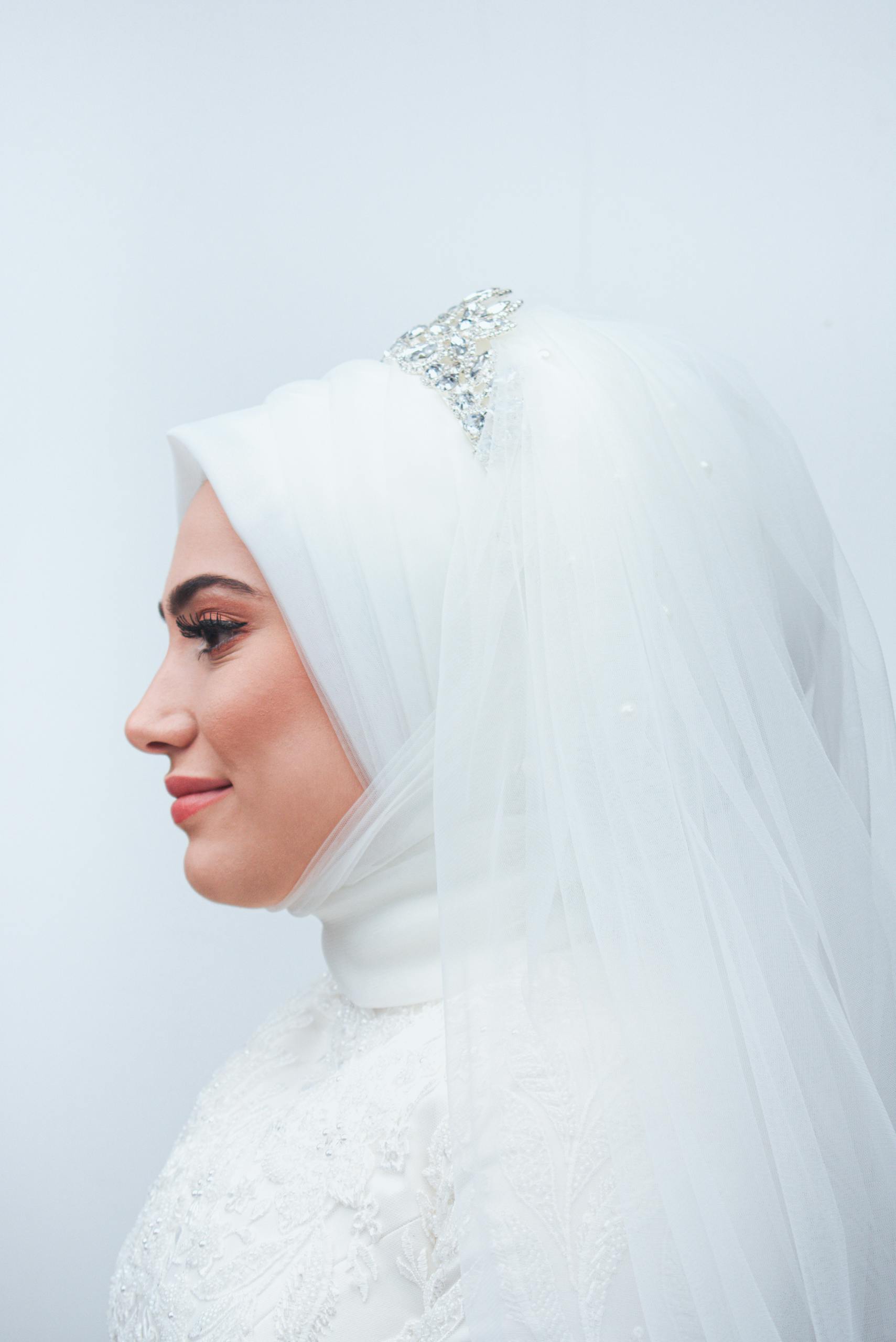 Profile portrait of a hijabi bride in a detailed white wedding dress.
